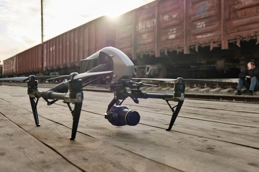 A professional drone stands on a wooden floor, preparing for flight and cinema shoot, old train on background