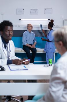 Healthcare facility nurse examining x-ray scan image of elderly patient with acute leg pain. Retired man listening to nurse talking about consultation appointment and treatment schedule