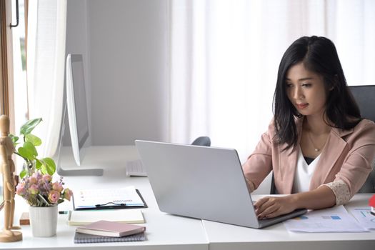 Pretty millennial woman sitting in modern office and using computer laptop.