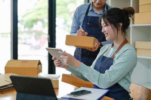 Asian couple doing online business together at home. Helping to pack products into cardboard boxes. family concept, modern business, small entrepreneurs, online delivery.