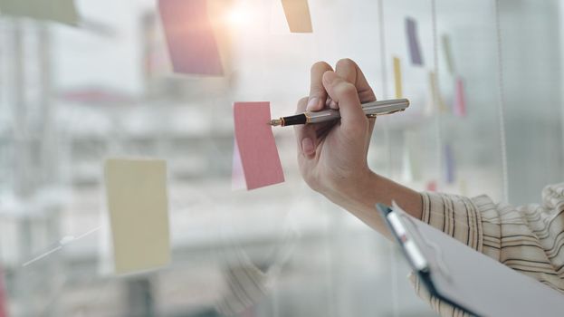 Businessman writing new idea on sticky notes at bright modern office.