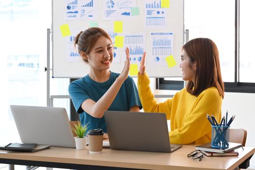 Two happy colleagues giving high fives each other to celebrate corporate success.