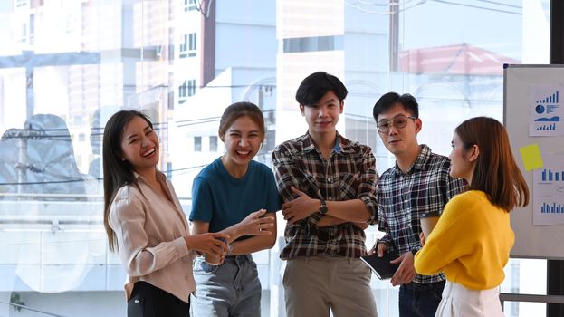 Successful business team standing near large window at office with city buildings in background.