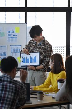 Young asian male holding digital tablet and giving presenting new marketing strategy in meeting.