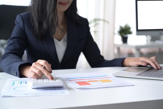 Professional investor using calculator and checking financial reports at her workplace.