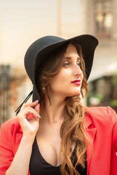 Side view of fashionable young woman in red coat and black hat looking away on the city street.