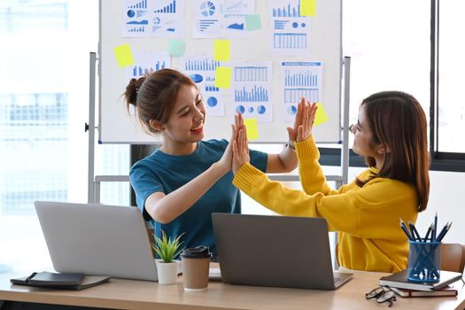 Young business people giving high fives each other for celebrating victory together.