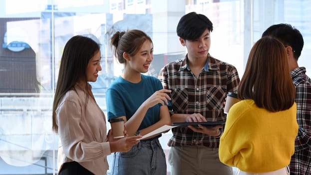 Young businesspeople discussing start up project together while standing near large window in office.