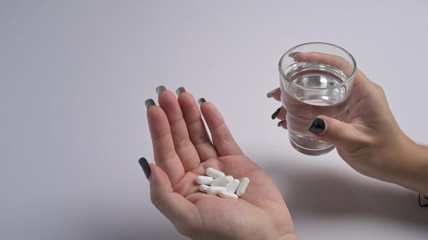 Woman holding pills and a glass of water in hand. Healthcare, medicine, treatment, therapy concept.