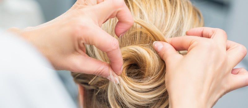 Close up rear view of hairdresser making hairstyle for long hair of blonde woman.