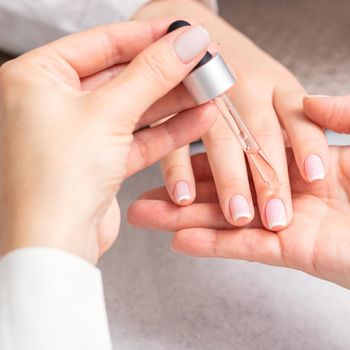 Professional manicurist pouring oil on nails french manicure of woman in beauty salon.