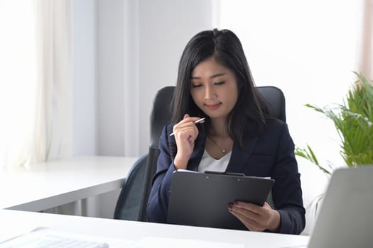 Millennial businesswoman sitting in bright office and reading financial reports.