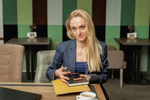 Portrait of beautiful young business woman holding office supplies sitting in office.