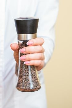 Female hands holding pepper mills wearing white shirt on yellow background.