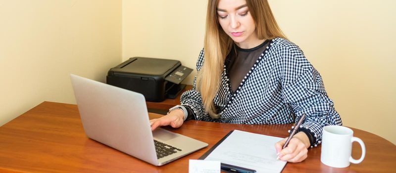 Business woman is writing on a document with laptop at home office.