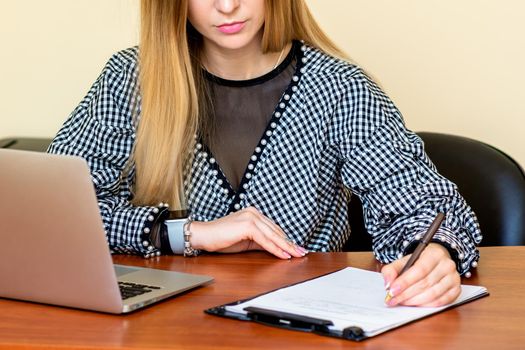 Business woman is writing on a document with laptop at home office.