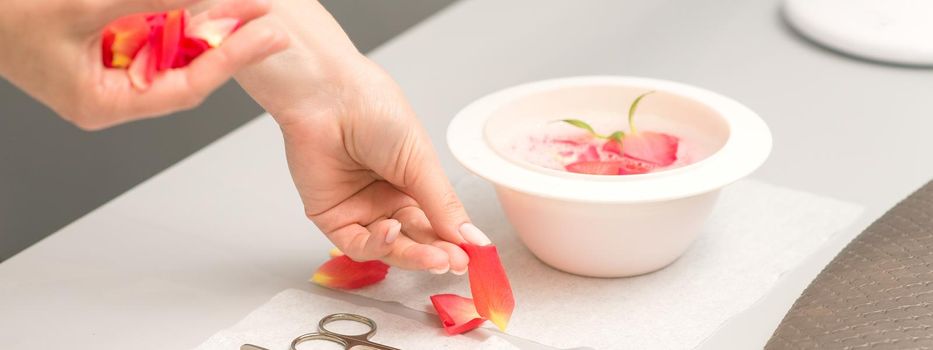 Hands of manicurist decorates bowl of water and table with petals in spa.