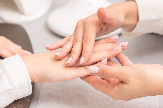Hands and nails of young woman receiving oil massage by beautician at beauty salon.