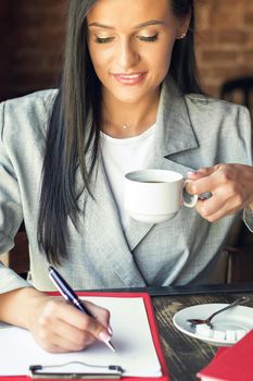 young businesswoman is writing plans on the notebook while holding cup of coffee at cafe, business concept