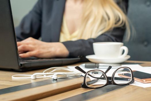 Eyeglass with coffee on office table on female business worker background.