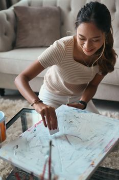 Happy millennial woman in casual clothes sitting in living room and enjoy creating her artwork.