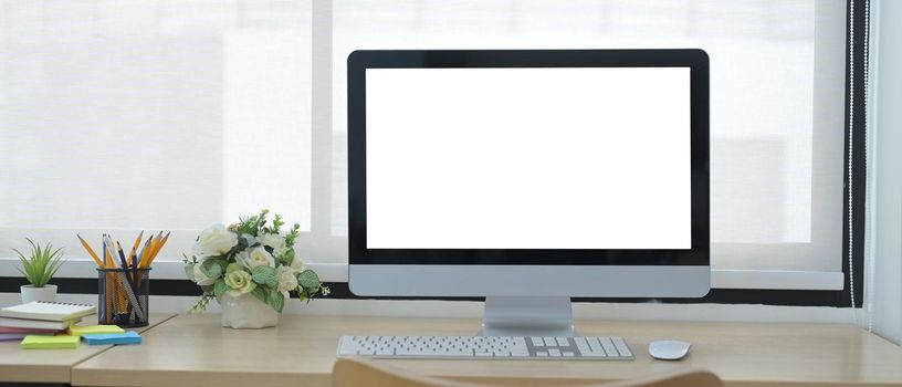 Front view computer pc with blank screen, flower pot and supplies on wooden table.