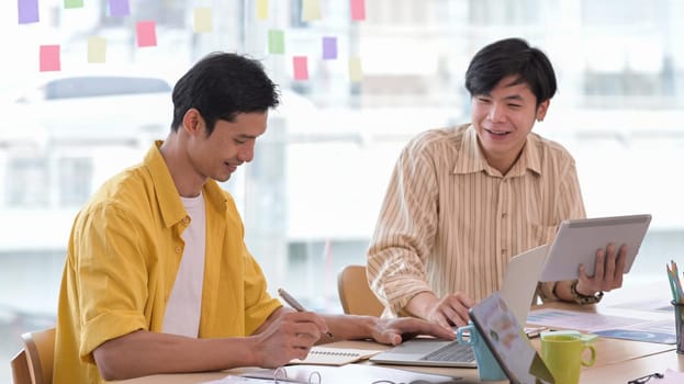 Two happy young creative man working together at modern workplace.