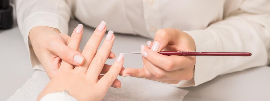 Hand of young woman receiving french manicure by beautician at nail salon.