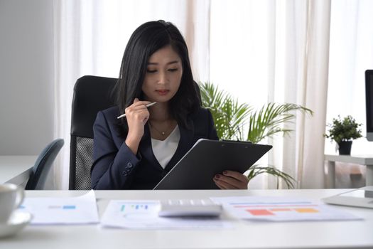 Concentrated young businesswoman analyzing financial document at office desk.