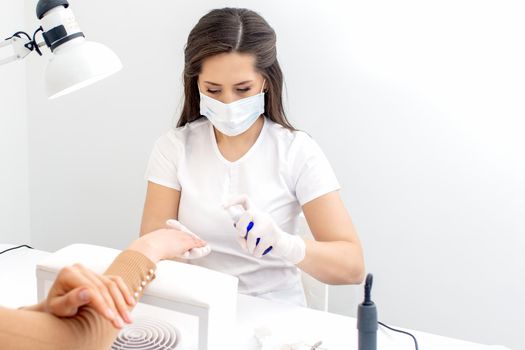 Manicurist is applying spray on client hand. Manicure disinfection with spray.