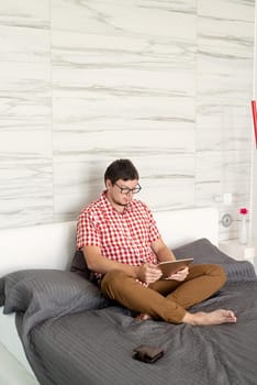 Online shopping concept. Young man sitting on the bed and shopping online using tablet