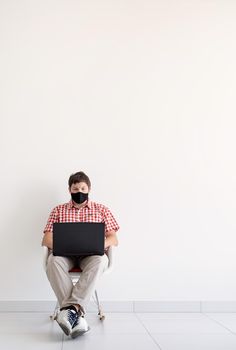 Social distancing. E-learning. Young man in black protective mask using laptop, sitting at the chair. Copy space