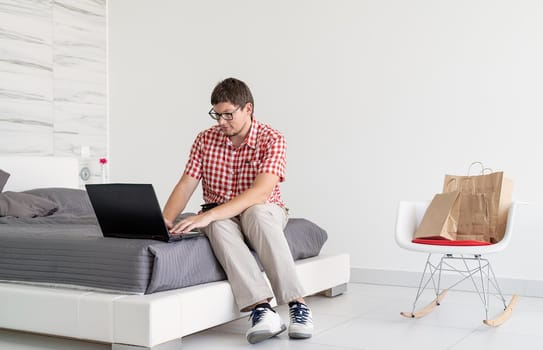 Online shopping concept. Young man sitting on the bed and shopping online using tablet