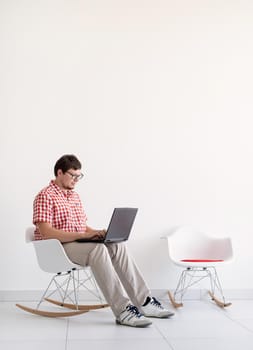 Online shopping concept. Young man sitting in the chair and shopping online using laptop looking at the credit card, copy space