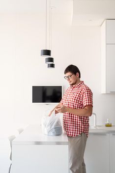 Delivery food, products to home. Shopping and healthy food concept. Young man in red plaid shirt holding a disposable plastic bag with food delivery at the modern kitchen