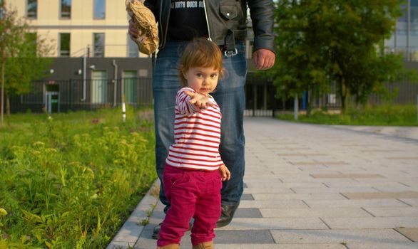 Funny daughter and her father. Little baby girl is walking in the park. Brutal father in biker jacket walking behind