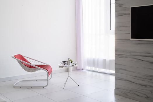 Minimal light and airy interior. White living room with red leather chair and coffee table