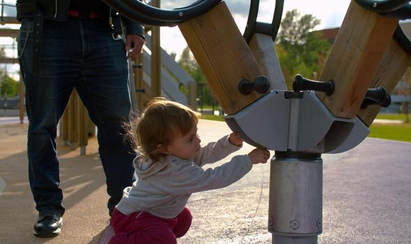 Baby girl exploring carousel in the park. Back light.