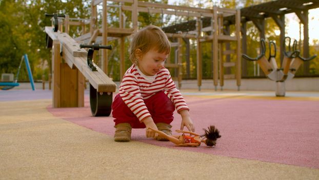 Little girl on the playground in the park playing with a doll. Good sunny day