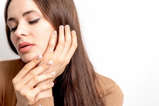 Portrait of pretty young woman touching face with her hand beige manicure on white background with copy space.