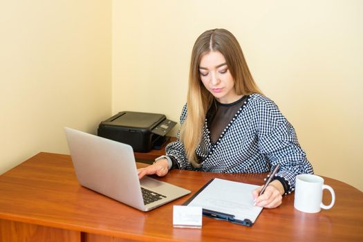 Business woman is writing on a document with laptop at home office.