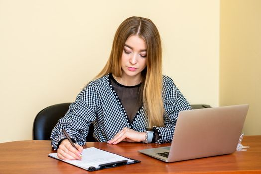 Business woman is writing on a document with laptop at home office.