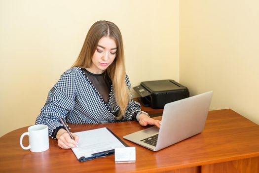 Business woman is writing on a document with laptop at home office.