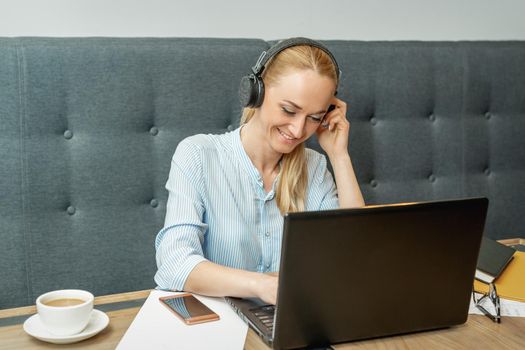 Happy young woman wearing headphones looking on laptop screen during online training and video conference at home office.