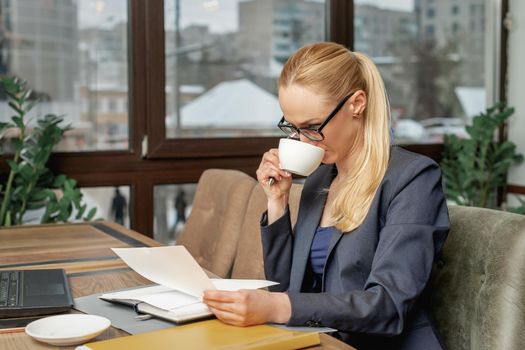 Business woman reading news working with documents and drinking coffee in office.