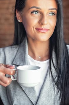 Portrait of young woman is holding cup of coffee, smiling at coffee shop cafe. Woman with white cup of coffee.