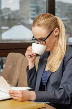 Business woman reading news working with documents and drinking coffee in office.