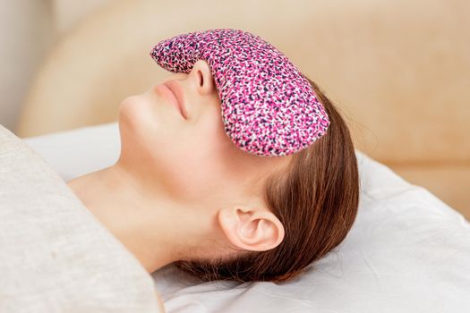 Woman is relaxing with restorative eye pillow on her eyes on bed.