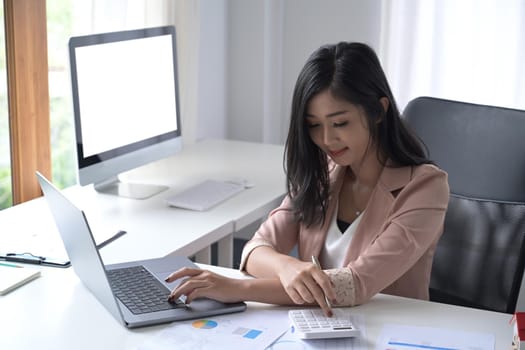 Thoughtful businesswoman using calculator and preparing annual financial report at workplace.