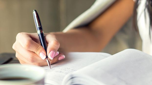 Young woman right hand writing plans on small diary in cafe close up. Business concept